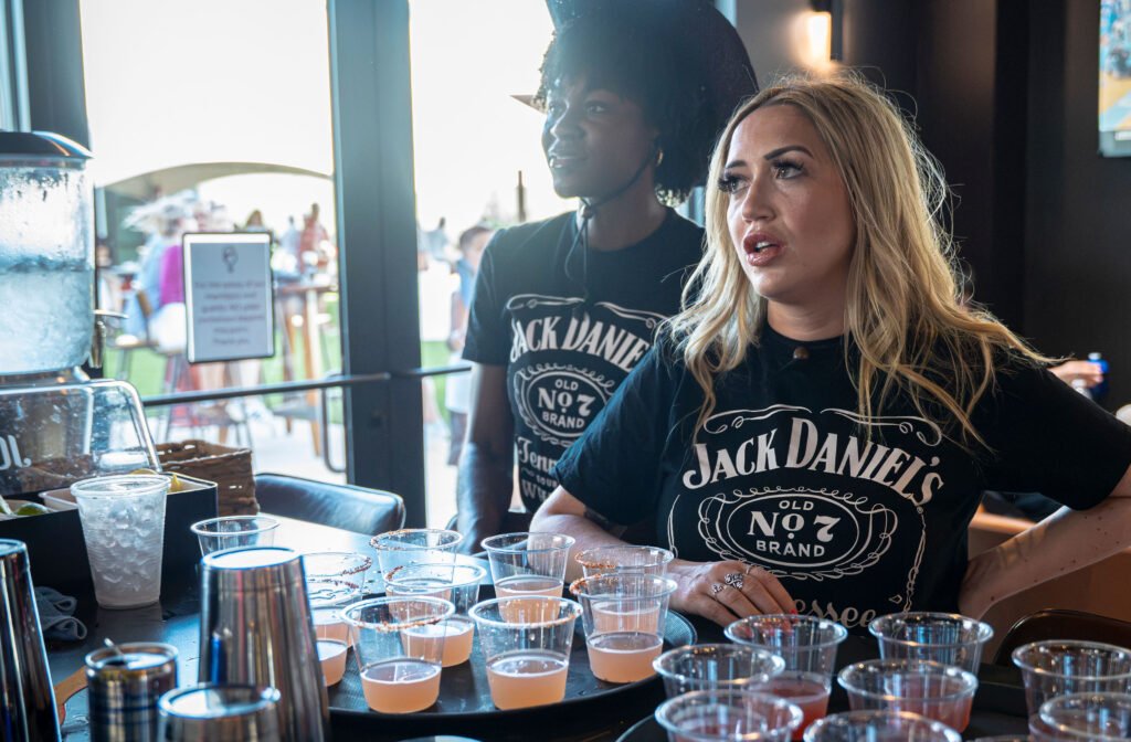 Bartenders behind the bar preparing tasting sample cups and shots during an event at The Bench sports bar in Fort Worth