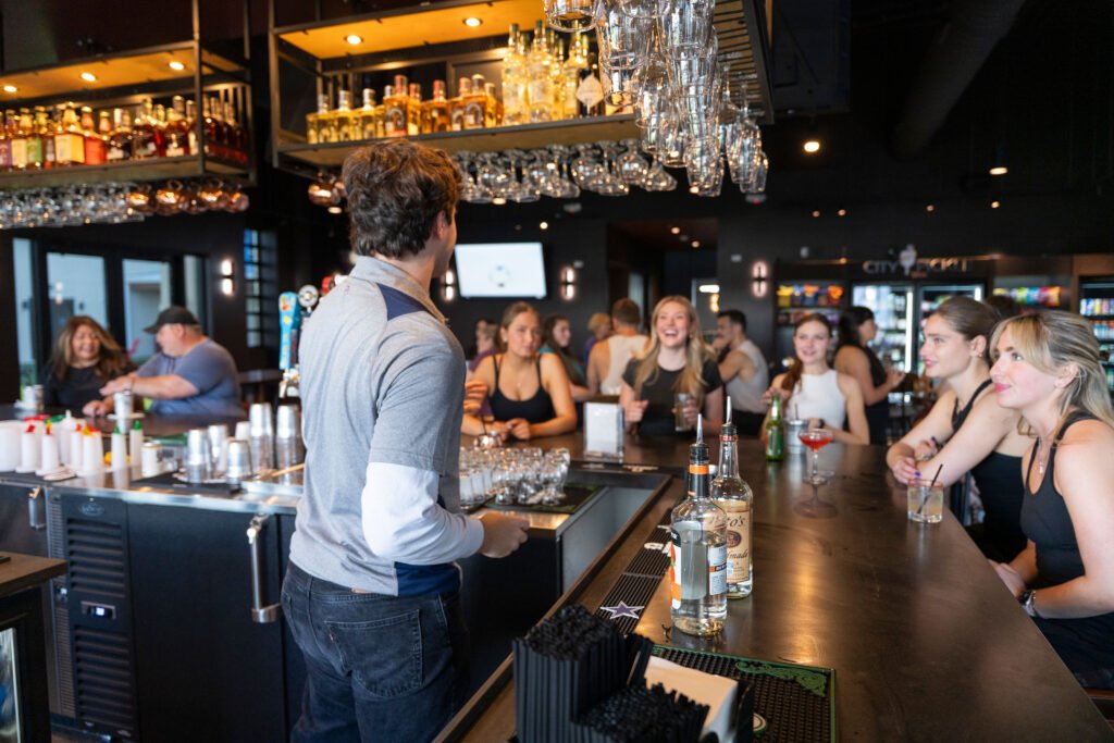 Bartender serving guests and socializing across the counter at the full service bar inside The Bench Fort Worth