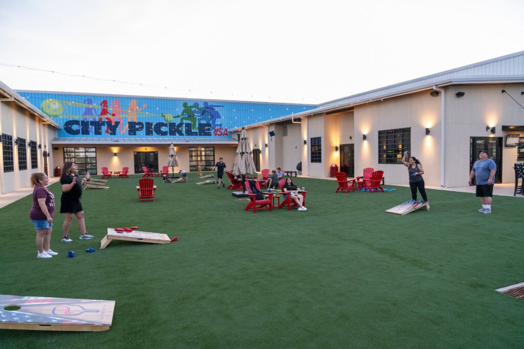 Wide view of the outdoor artificial turf courtyard with lawn games and seating outside City Pickle USA and The Bench Fort Worth