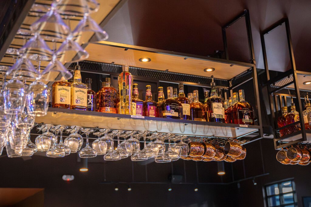 Overhead bar shelf display featuring premium liquor bottles, hanging glassware, and copper mugs at The Bench Fort Worth