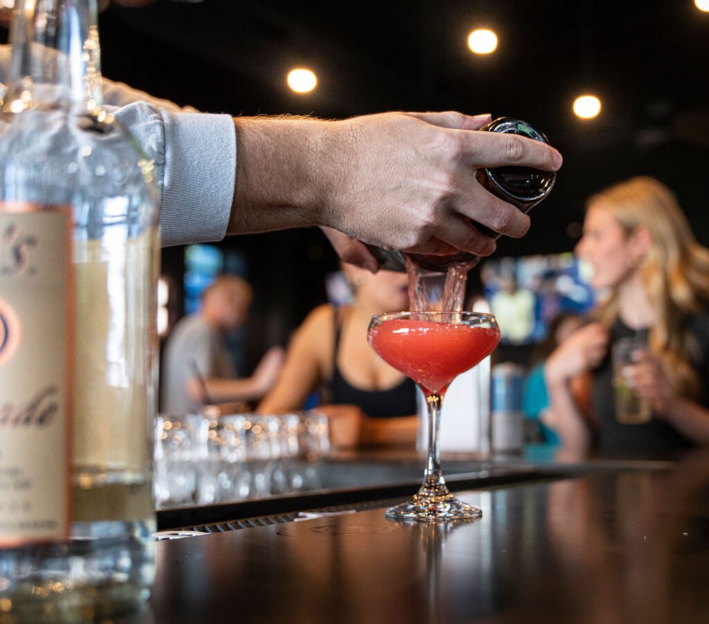 Bartender shaking and pouring a pink craft cocktail at The Bench sports bar in Fort Worth
