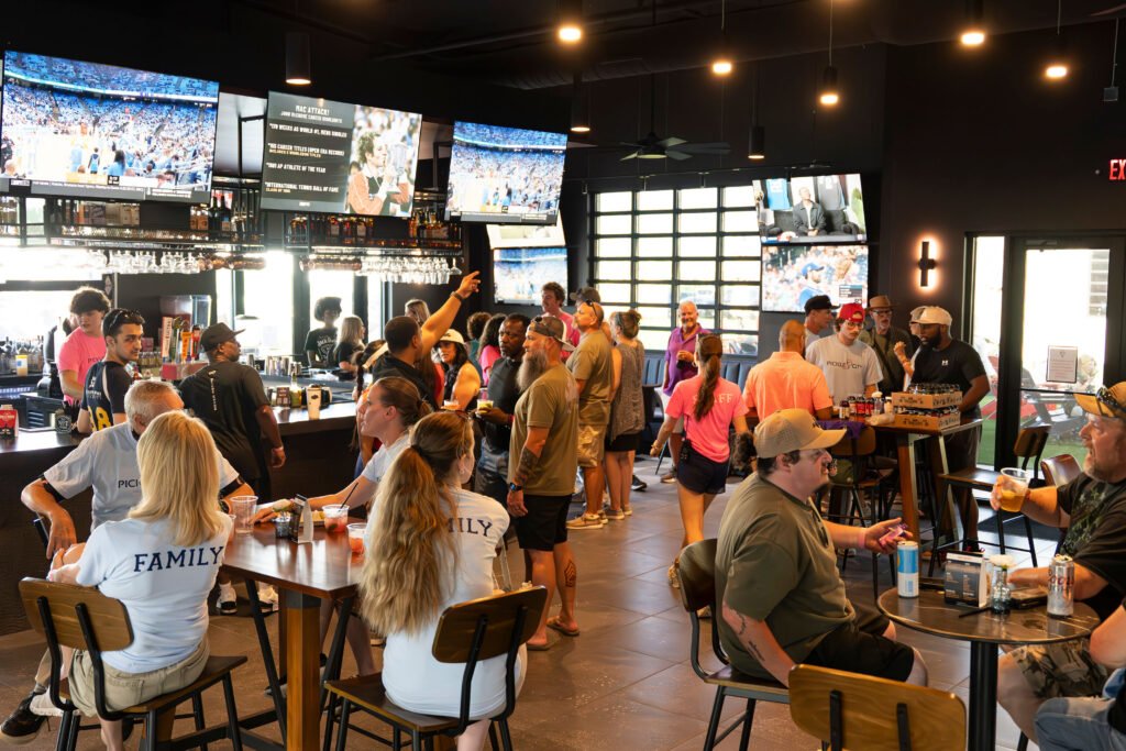 Crowd gathering inside The Bench sports bar in Fort Worth watching sports on multiple wall-mounted TV screens