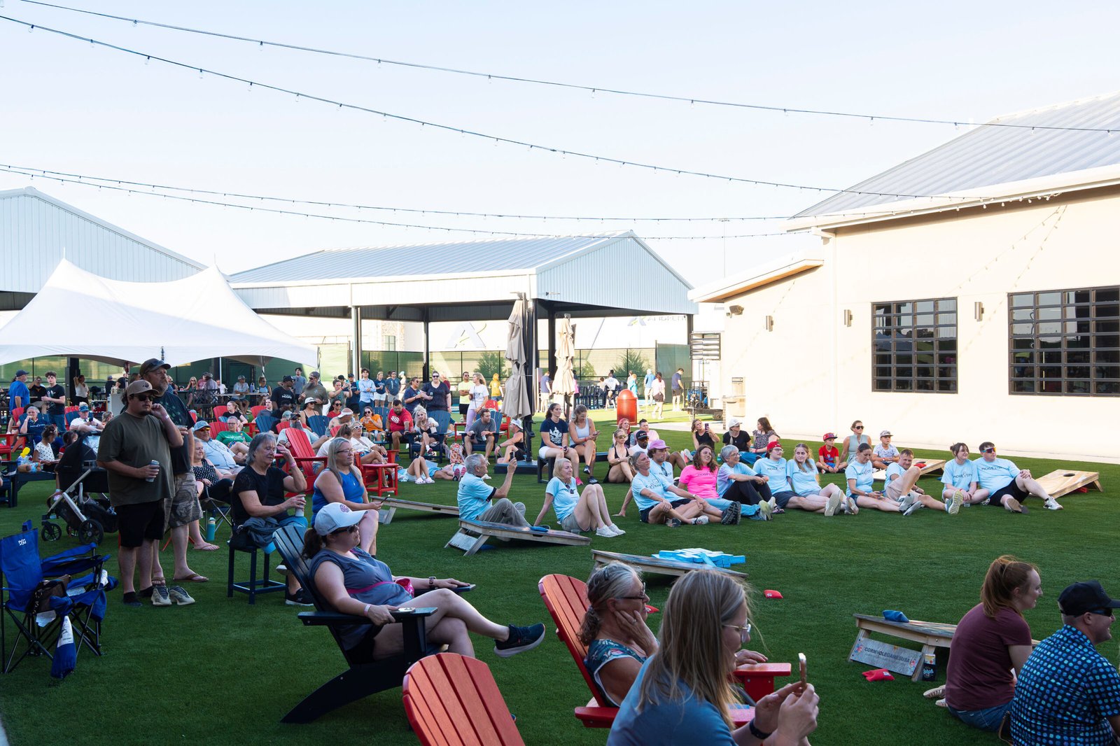 Large crowd seated across the artificial turf lawn for an outdoor community event and watch party outside The Bench sports bar in Fort Worth